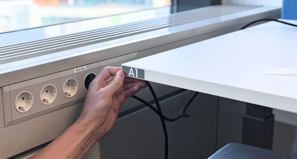 Kuvassa asennetaan merkintäteippiä työpisteen pöydän reunaan.