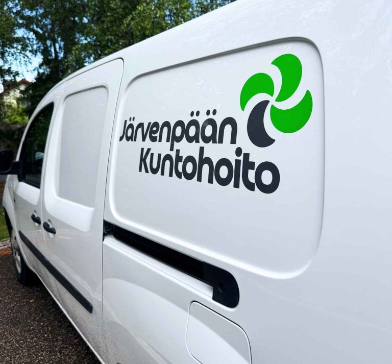 Pakettiauton sivuteippaus, jossa näkyy yrityksen logo ja nimi selkeästi valkoisella pinnalla.